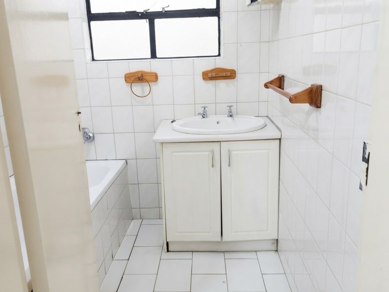 A functional bathroom featuring a vanity cabinet, ceramic basin, and bathtub with white wall and floor tiling.