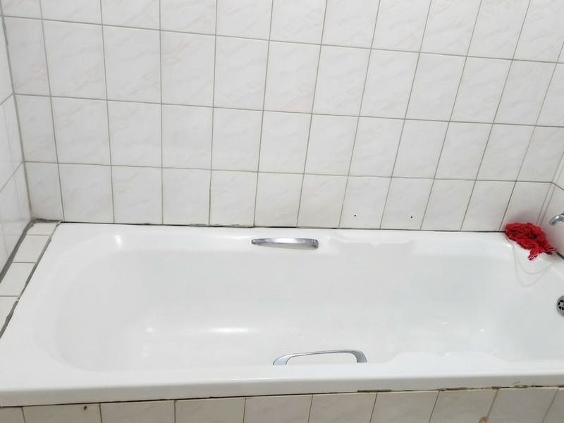 A functional bathroom featuring a built-in bathtub with chrome fixtures and white ceramic wall tiling.