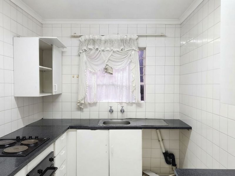 A functional kitchen featuring built-in cabinetry, laminate countertops, a stainless steel sink, and an integrated electric hob and oven with tiled wall finishes.
