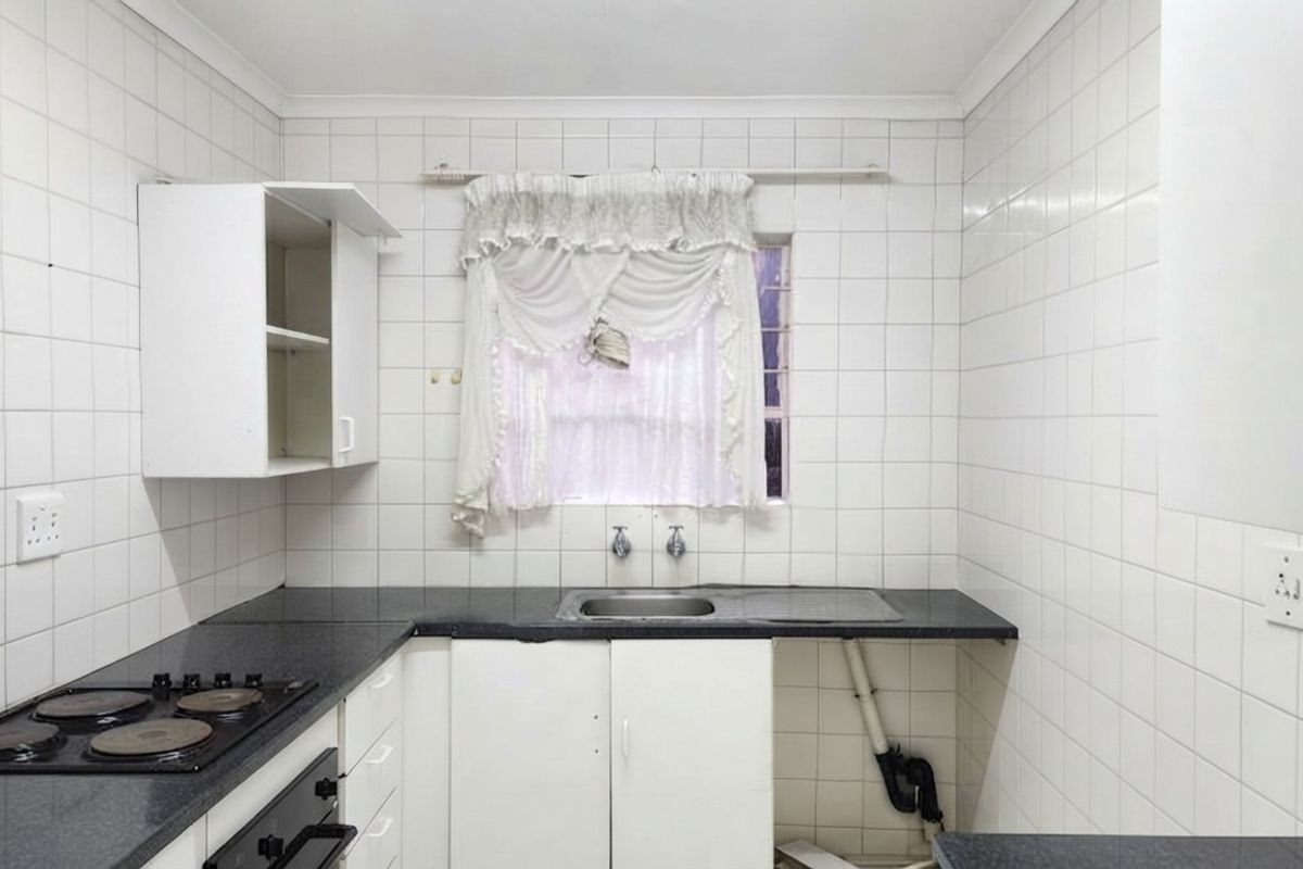 A functional kitchen featuring built-in cabinetry, laminate countertops, a stainless steel sink, and an integrated electric hob and oven with tiled wall finishes.