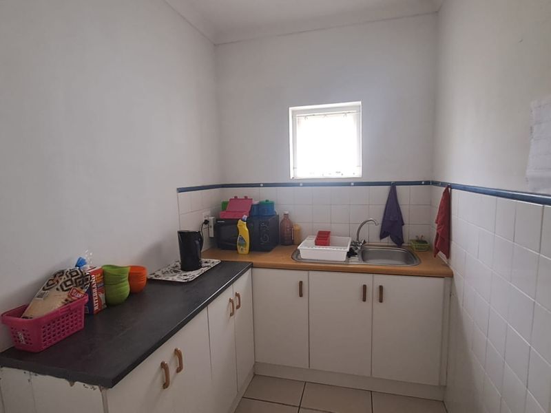 A functional scullery or kitchenette area featuring built-in cabinetry, a stainless steel sink, and tiled splashbacks, providing practical utility space.