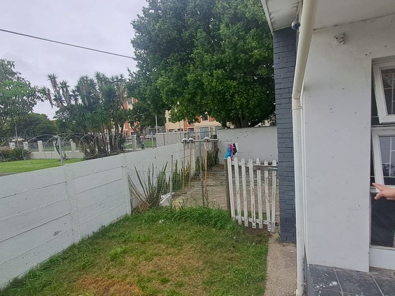 Rear exterior area featuring a precast concrete boundary wall with razor wire, a paved walkway, and a small garden section.