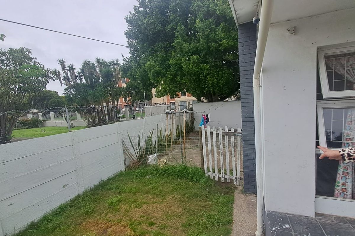 Rear exterior area featuring a precast concrete boundary wall with razor wire, a paved walkway, and a small garden section.