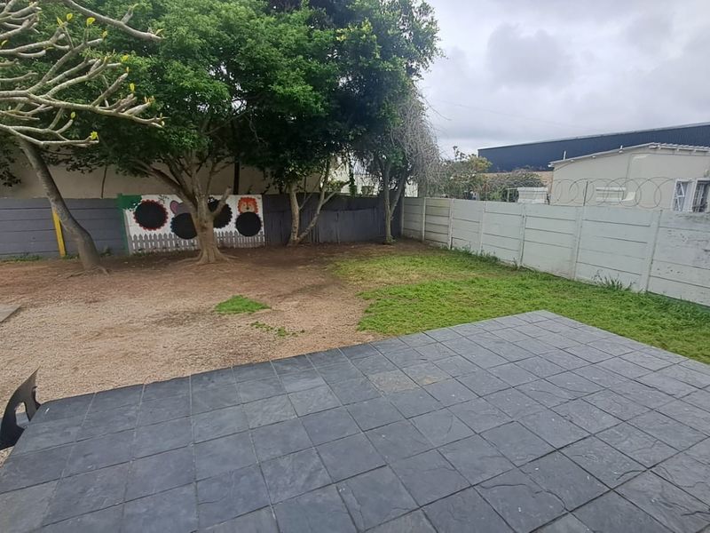 A rear outdoor area featuring a paved patio, a precast concrete boundary wall with security razor wire, and established trees.