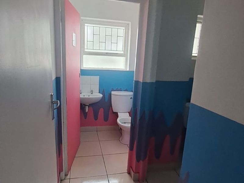 A small bathroom featuring tiled flooring, a standard toilet, and a wall-mounted basin, currently finished with non-standard decorative wall paint.