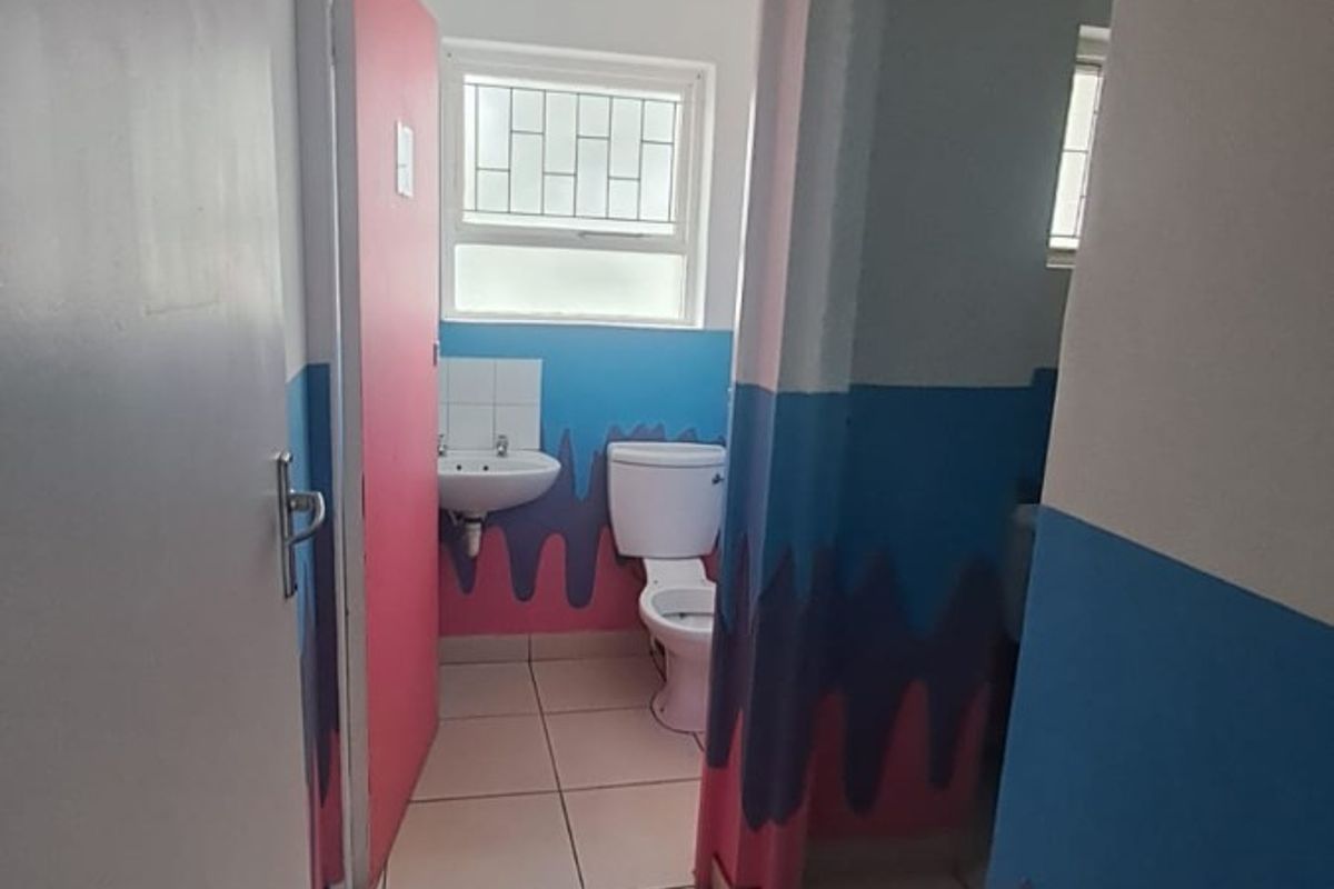 A small bathroom featuring tiled flooring, a standard toilet, and a wall-mounted basin, currently finished with non-standard decorative wall paint.