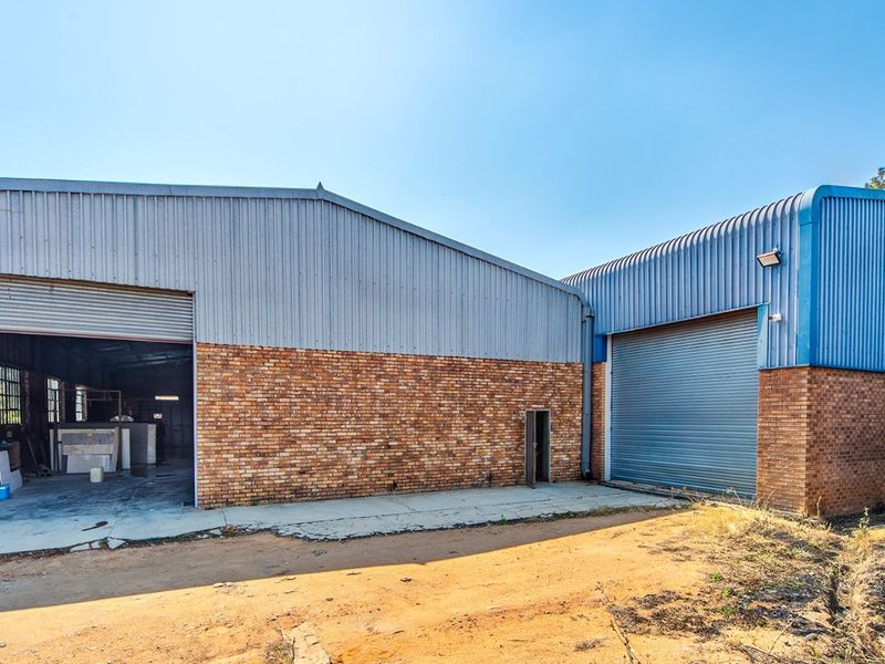 Industrial warehouse facility featuring face brick and corrugated metal construction with large roller shutter access doors and a concrete apron.