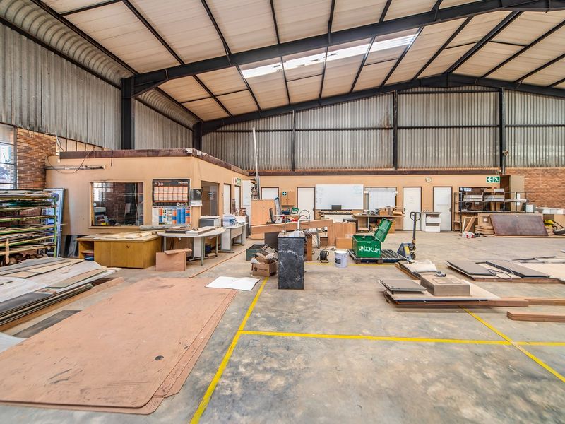 Spacious industrial warehouse area featuring high ceilings with exposed steel trusses, corrugated metal cladding, concrete flooring, and an integrated internal office structure.