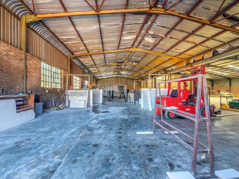 Spacious industrial warehouse featuring exposed brick walls, concrete flooring, and a high-clearance steel truss roof structure with visible insulation damage.
