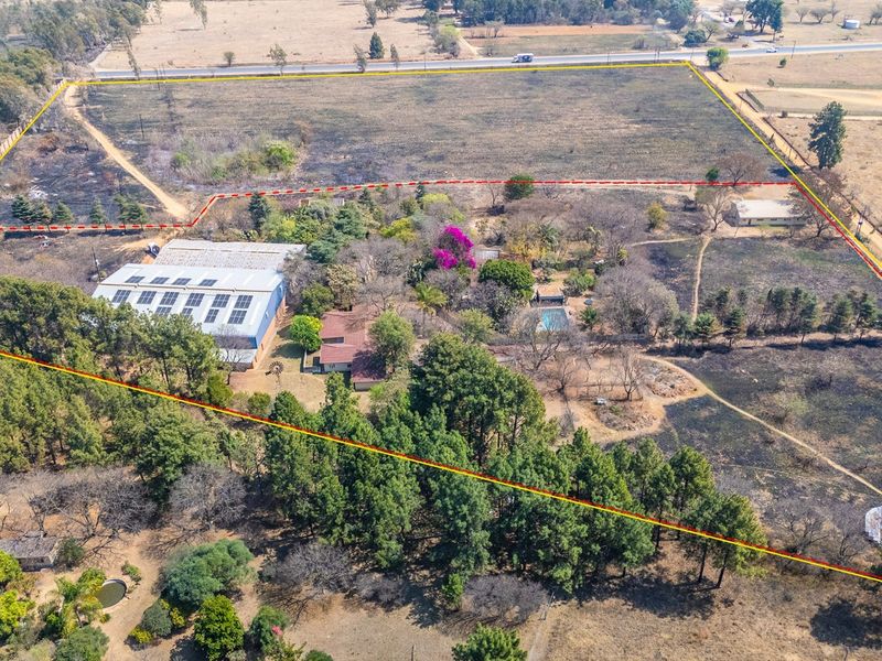 Aerial view of a large industrial property featuring a warehouse with solar panels, a swimming pool, and extensive grounds with mature trees.