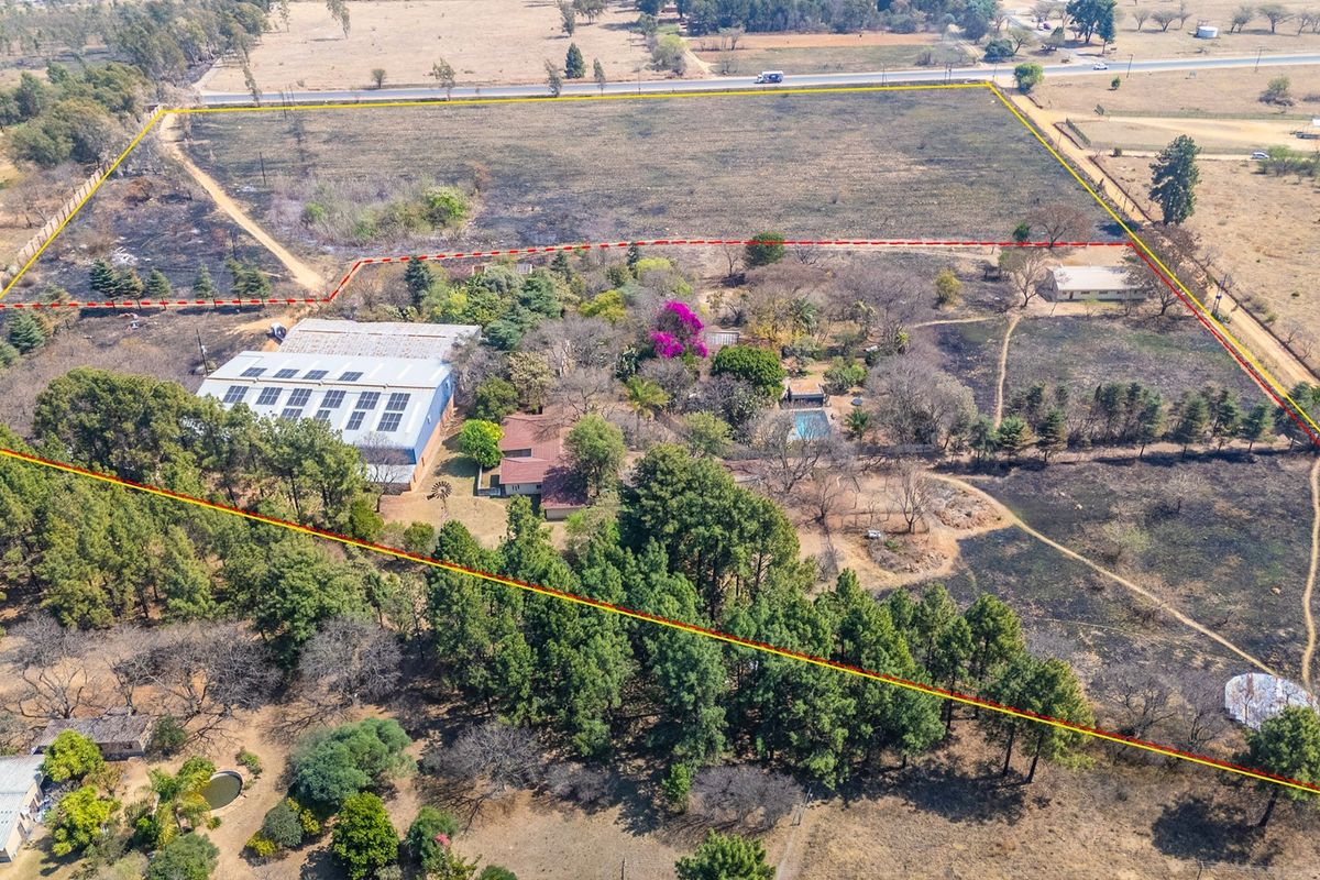 Aerial view of a large industrial property featuring a warehouse with solar panels, a swimming pool, and extensive grounds with mature trees.