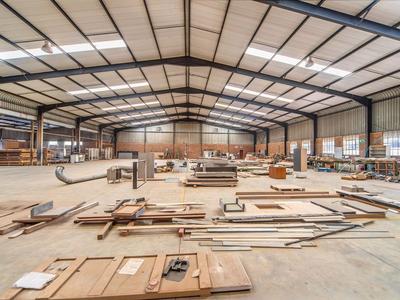 Spacious industrial warehouse featuring a high steel portal frame, concrete flooring, and natural light through integrated skylights, suitable for manufacturing or storage.
