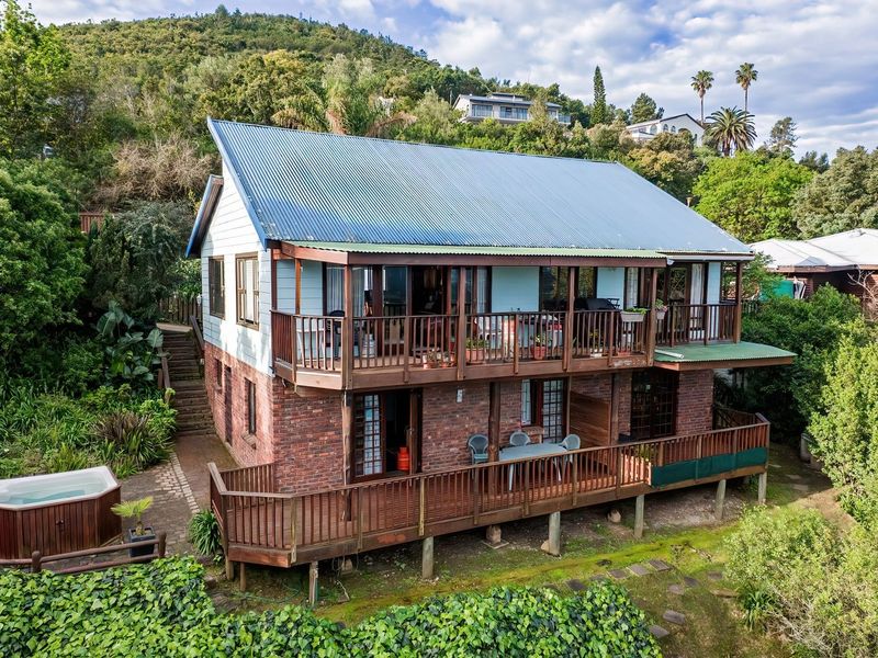 Rear view of a two-story house featuring timber decks, brick lower level, metal roof, and an outdoor hot tub set in a landscaped garden.