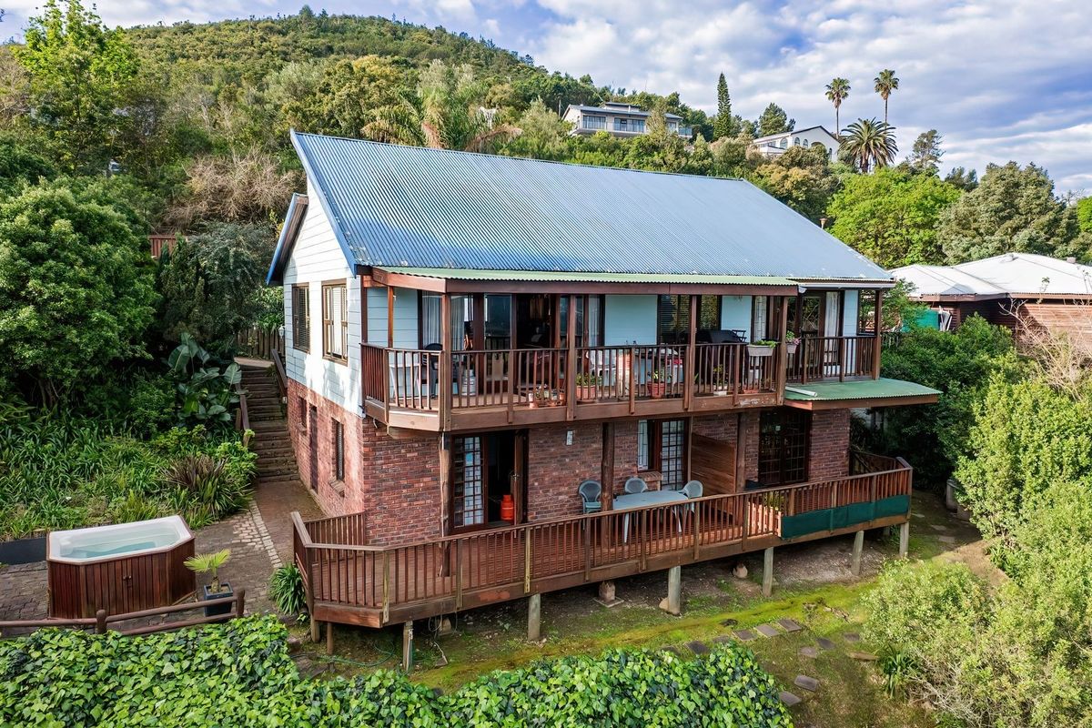 Rear view of a two-story house featuring timber decks, brick lower level, metal roof, and an outdoor hot tub set in a landscaped garden.