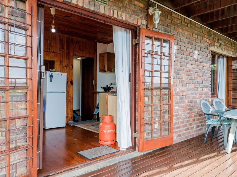 Covered patio area featuring exposed brick walls and timber decking, providing direct access to the interior living space through timber-framed glass doors.