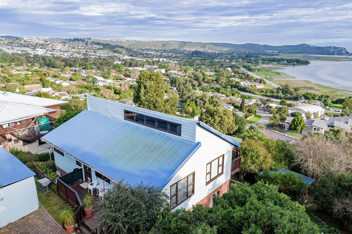Aerial view of a residential property featuring a corrugated metal roof, clerestory windows, and a timber deck, overlooking a coastal landscape.
