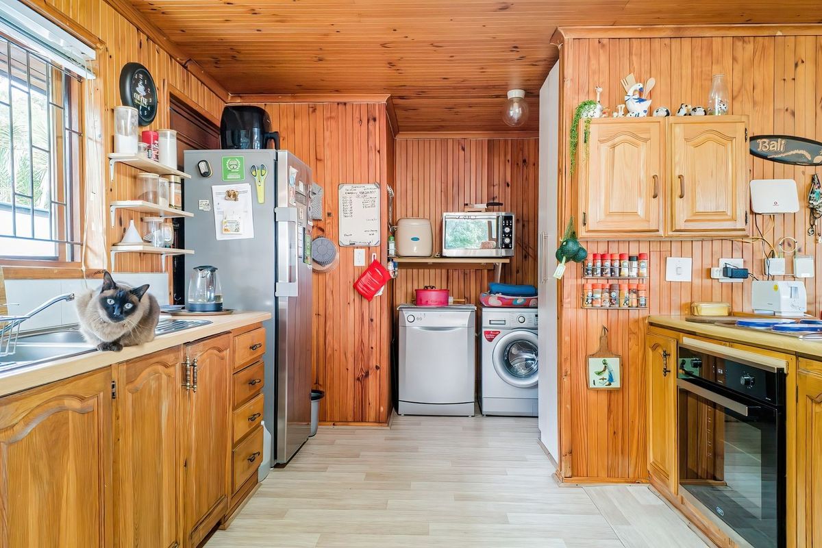 A functional kitchen featuring extensive timber wall and ceiling paneling, built-in wooden cabinetry, and integrated laundry appliances.