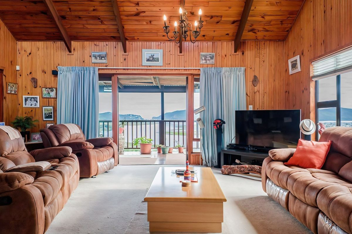 Spacious living room featuring warm timber wall paneling, exposed vaulted ceiling beams, and large sliding doors opening onto a scenic balcony.