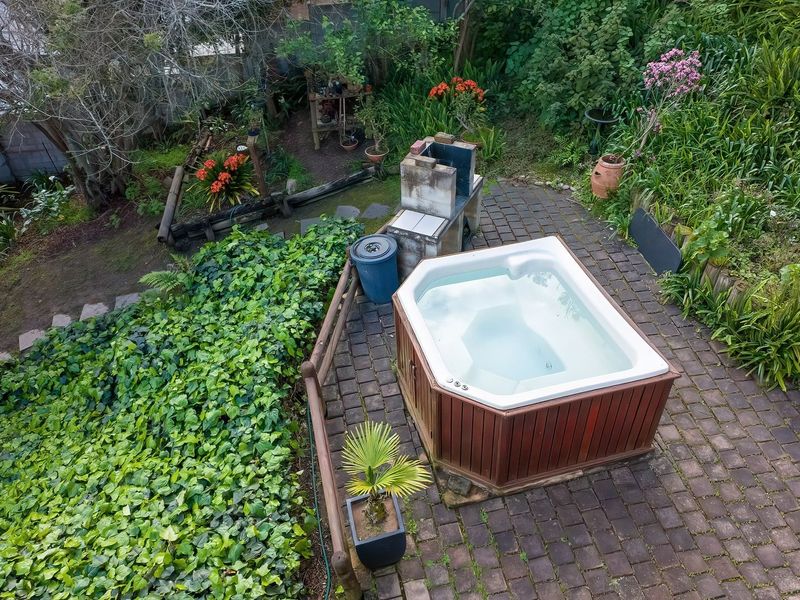An elevated view of a backyard featuring a paved patio area with a built-in braai and a hot tub set within a lush garden.