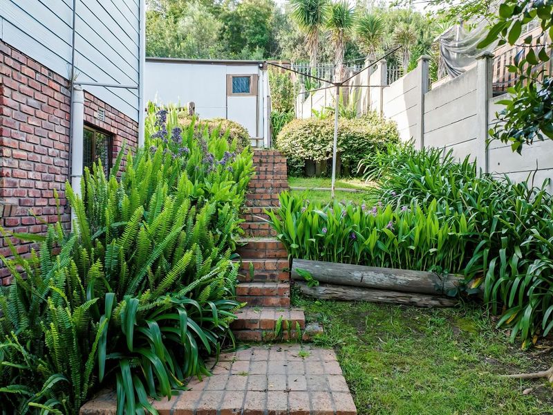 Rear garden area featuring brick stairs, paved pathways, and established landscaping with a precast concrete boundary wall.