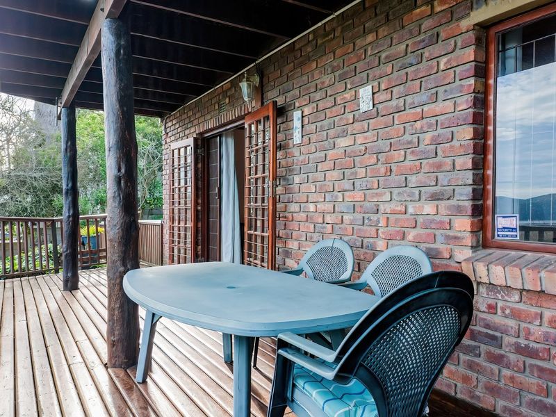 A covered outdoor patio featuring timber decking, exposed brick walls, and timber support posts, providing a rustic space for outdoor relaxation.