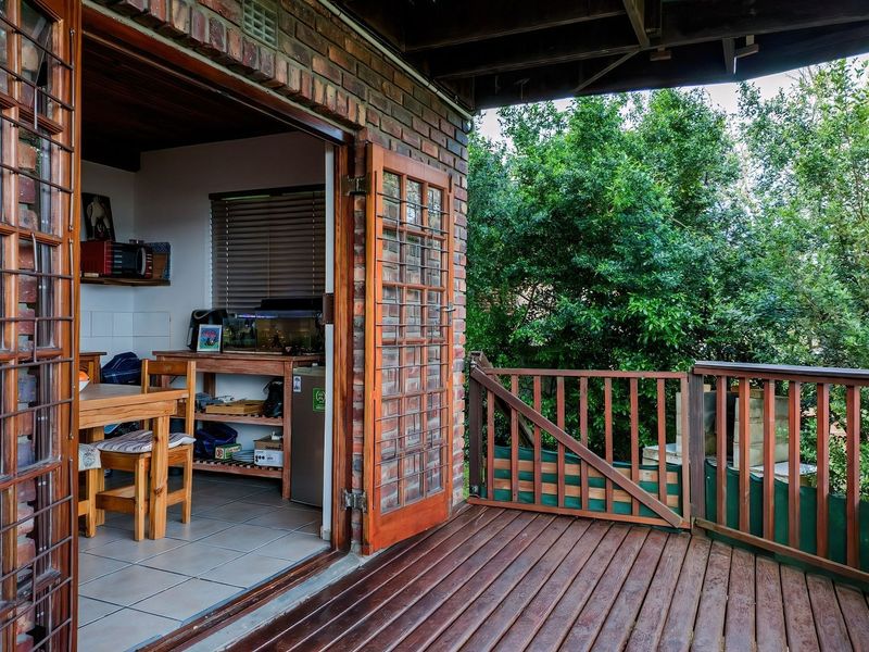 A covered timber deck patio featuring exposed brick walls and timber-framed glass doors, providing a seamless transition to the interior living space.