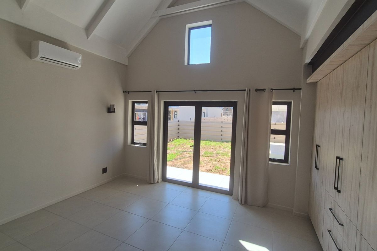 Spacious bedroom featuring a high vaulted ceiling, built-in cupboards, tiled flooring, and sliding glass doors providing direct access to the rear garden.