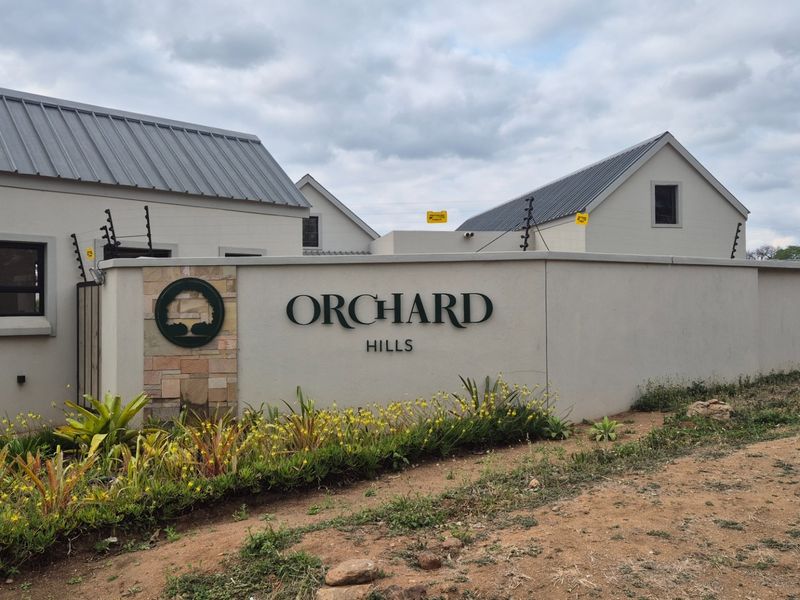 Entrance facade of Orchard Hills featuring a modern boundary wall, stone detailing, and secure electric fencing.