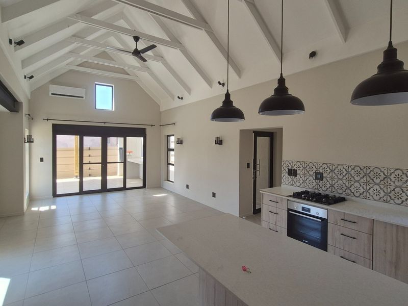Spacious open-plan living area featuring a vaulted ceiling with exposed rafters, modern kitchen with built-in appliances, and seamless access to the outdoor patio.