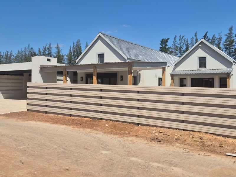 Modern residential property featuring a metal roof, timber pergola, and horizontal slat fencing, with a concrete driveway and covered carport area.