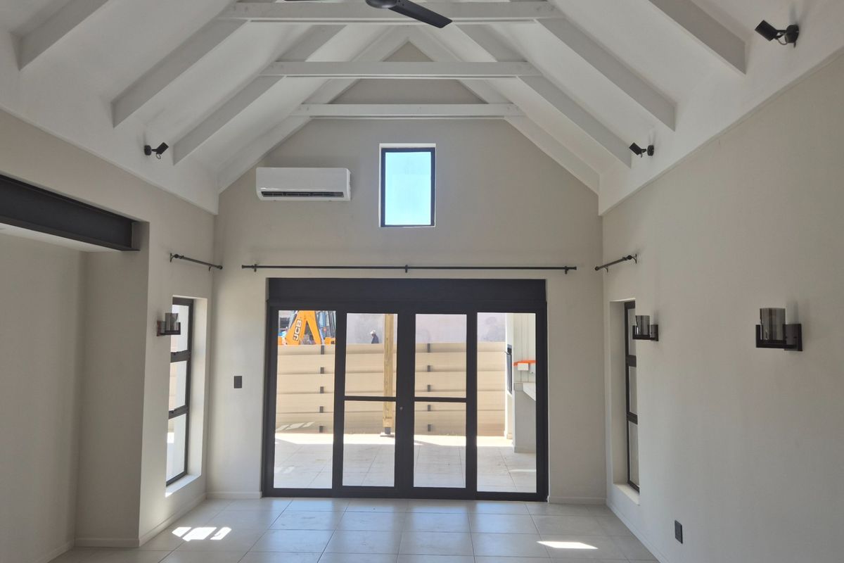 Spacious living area featuring a high vaulted ceiling with exposed rafters, tiled flooring, and large glass doors leading to an outdoor space.