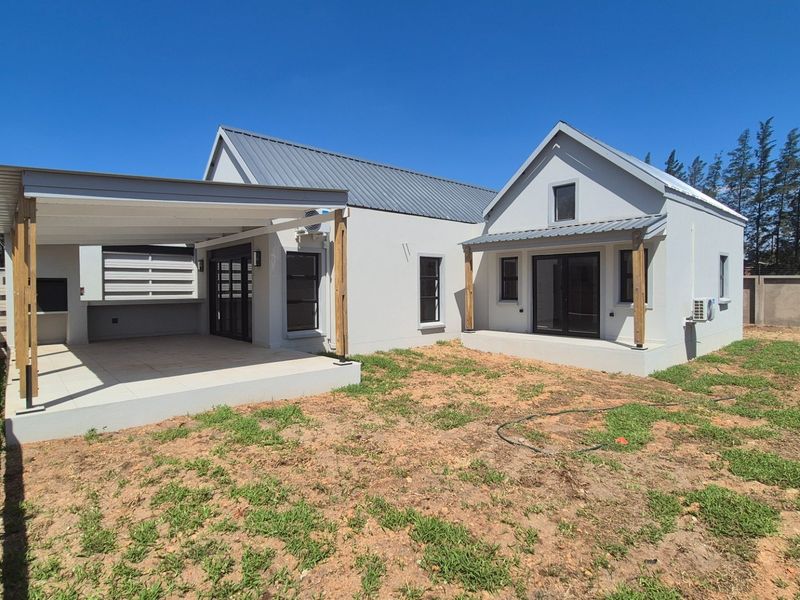 Rear view of a modern house featuring a covered patio with a built-in braai, sliding glass doors, and an expansive, unfinished garden area.