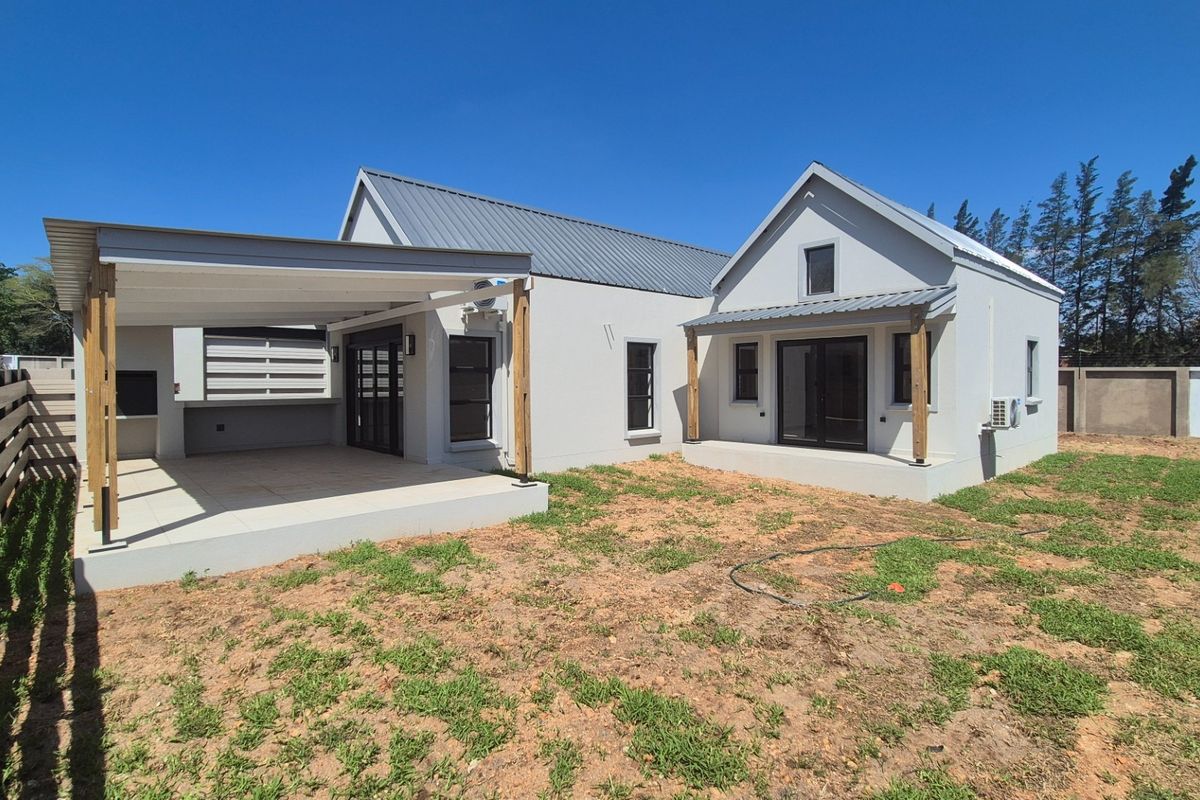 Rear view of a modern house featuring a covered patio with a built-in braai, sliding glass doors, and an expansive, unfinished garden area.