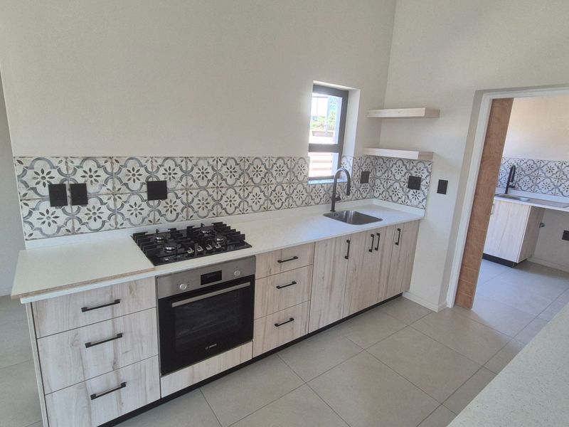 Modern kitchen featuring light wood cabinetry, stone countertops, a gas hob with built-in oven, and a decorative patterned tile backsplash.