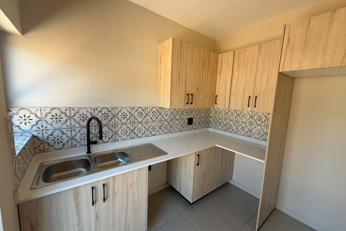Modern kitchen featuring light wood-look cabinetry, patterned tile backsplash, double stainless steel sink, and stone-look countertops in a clean, well-maintained space.