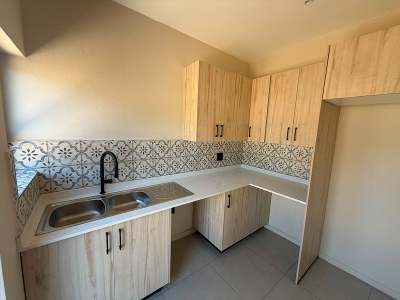 Modern kitchen featuring light wood-look cabinetry, patterned tile backsplash, double stainless steel sink, and stone-look countertops in a clean, well-maintained space.