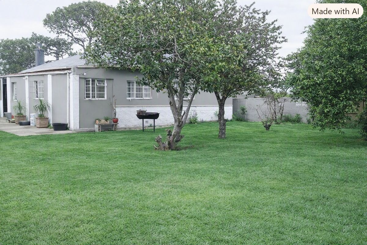 A view of the rear garden featuring a well-maintained lawn, mature trees, and a concrete patio area adjacent to the house exterior.