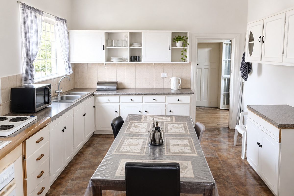 A functional kitchen featuring white cabinetry, laminate countertops, a double basin sink, and tiled flooring, offering a classic layout with potential for modernization.