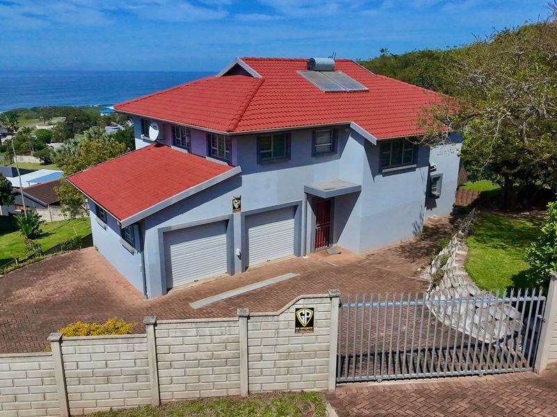 Aerial view of a double-story residential property featuring a tiled roof, solar water heater, paved driveway, and secure perimeter walling with a gated entrance.