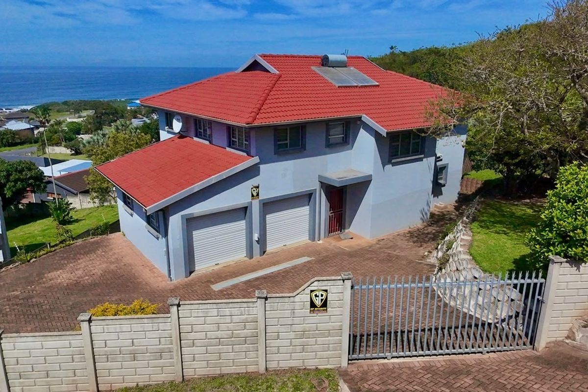 Aerial view of a double-story residential property featuring a tiled roof, solar water heater, paved driveway, and secure perimeter walling with a gated entrance.