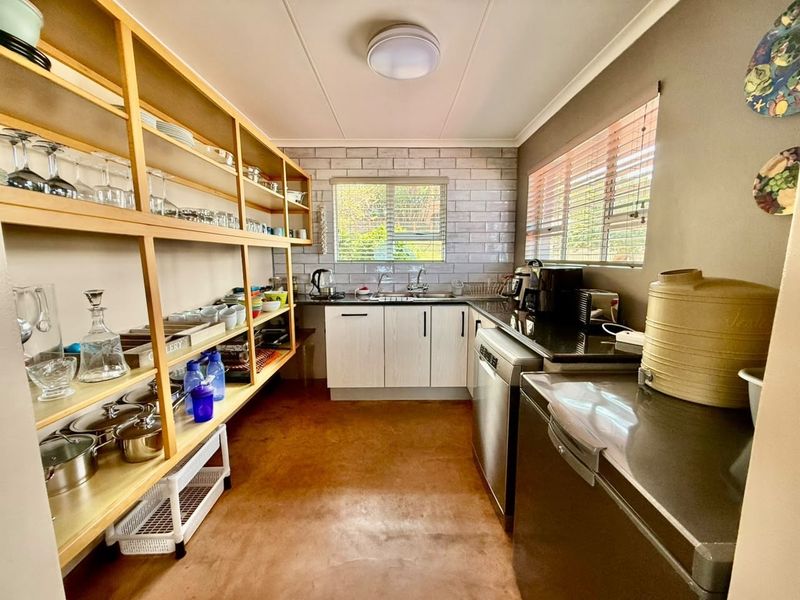 A functional scullery featuring extensive open shelving, granite countertops, subway tile backsplash, and a double basin sink for efficient food preparation and storage.