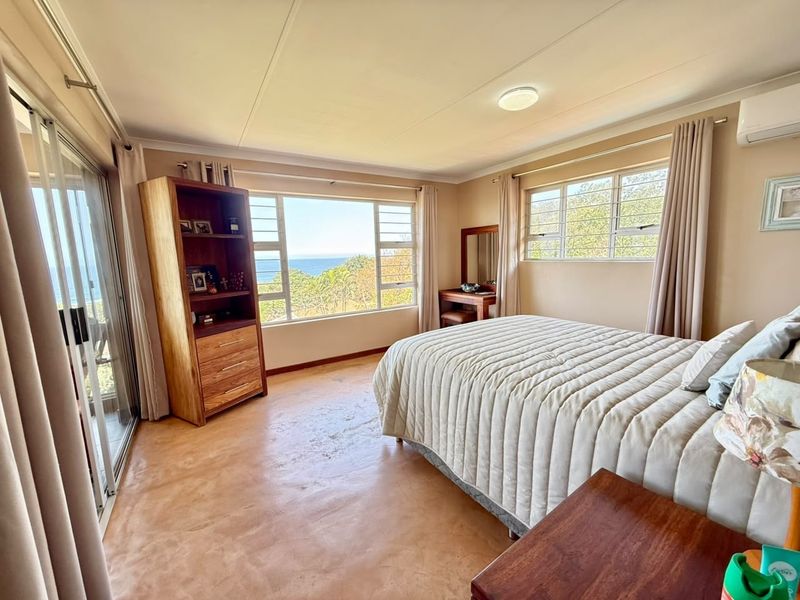 Spacious bedroom featuring polished concrete floors, air conditioning, and large windows offering scenic coastal views and natural light.