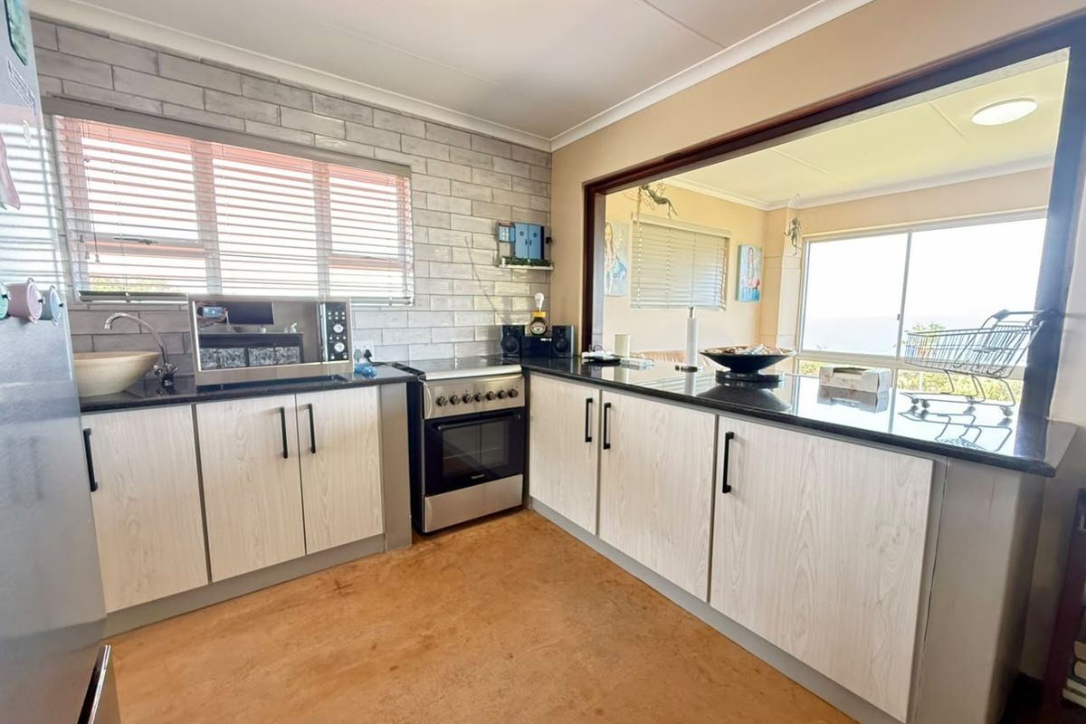Functional kitchen featuring light wood-grain cabinetry, dark granite countertops, a brick-style feature wall, and a convenient pass-through window overlooking the living area.