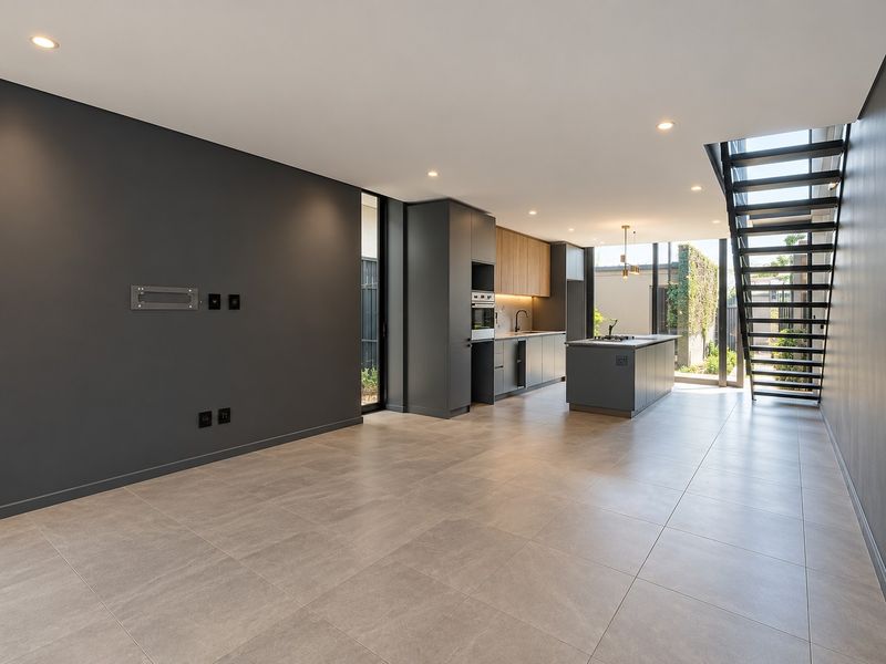 Modern open-plan living and kitchen area featuring sleek dark cabinetry, a central island, tiled flooring, and a striking architectural metal staircase.
