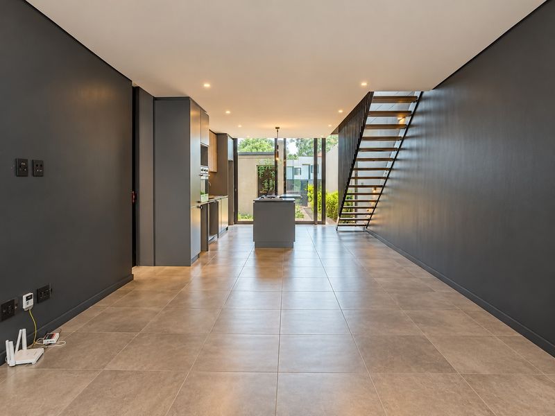 Modern open-plan living and kitchen area featuring dark cabinetry, a central island, tiled floors, and a contemporary staircase leading to the upper level.