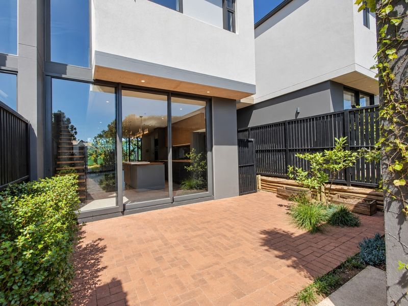 A modern rear townhouse exterior featuring a brick paved patio, sliding glass doors, and contemporary metal fencing.