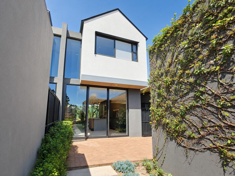 Modern townhouse rear elevation featuring large glass sliding doors, a paved patio area, and contemporary architectural design with climbing greenery.