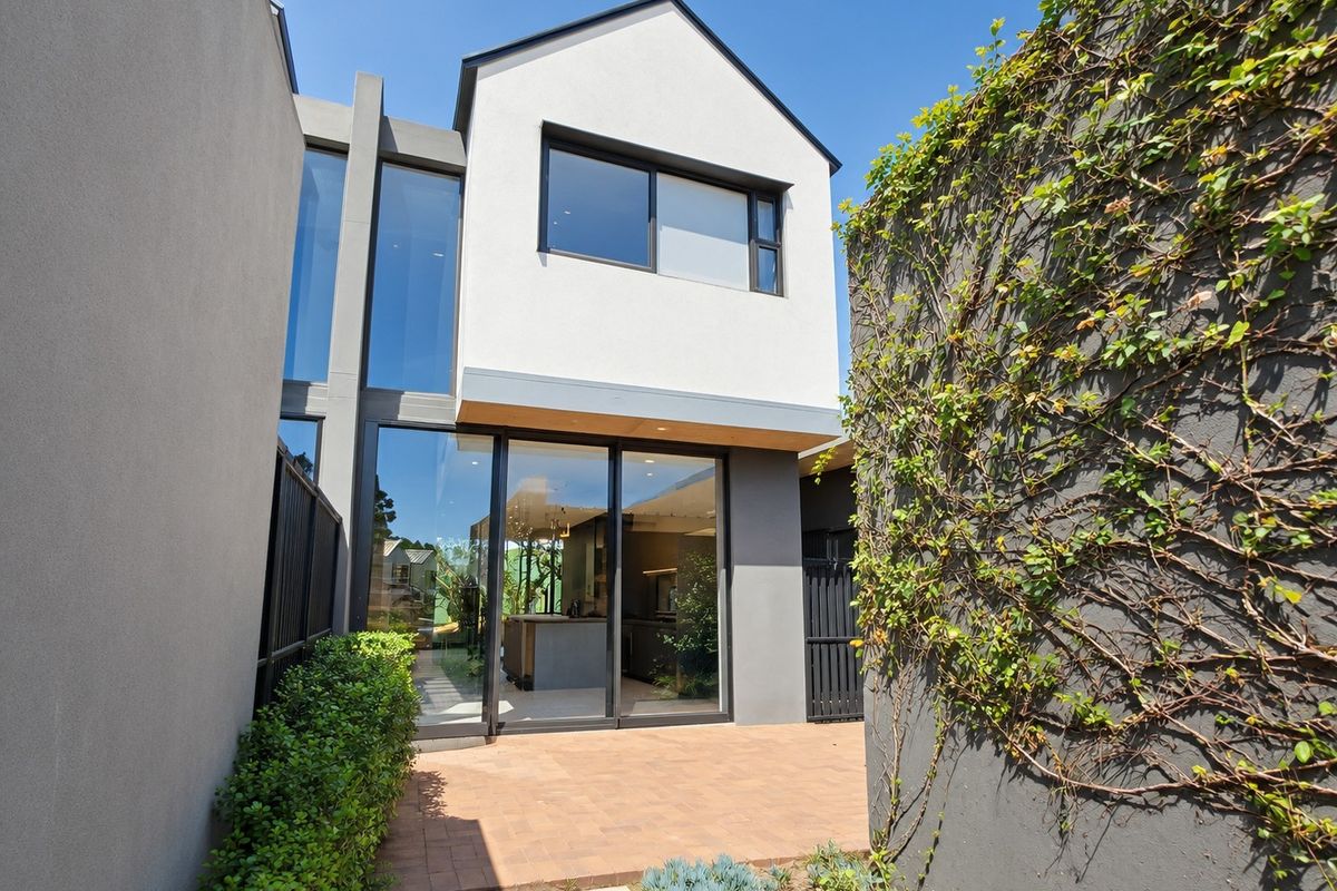 Modern townhouse rear elevation featuring large glass sliding doors, a paved patio area, and contemporary architectural design with climbing greenery.