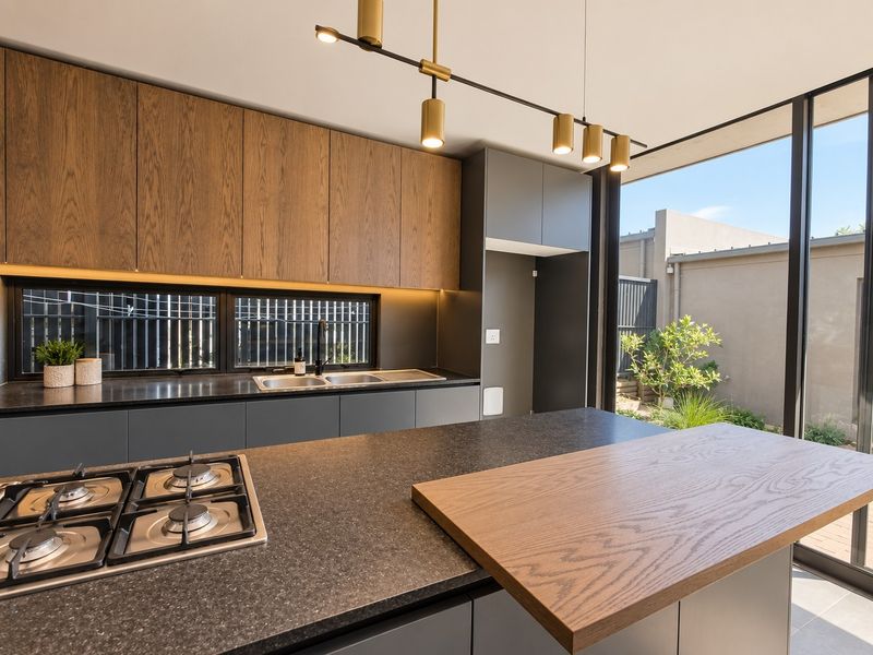 Modern kitchen featuring dark cabinetry, stone countertops, integrated gas cooktop, and large sliding glass doors opening to an outdoor area.