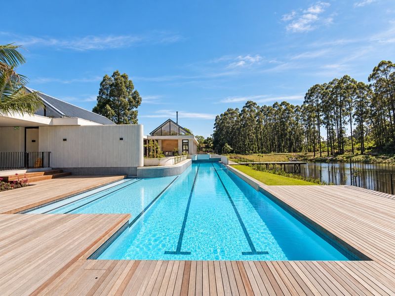 A pristine lap pool featuring extensive timber decking, modern architectural design, and scenic views of the surrounding landscape and water.